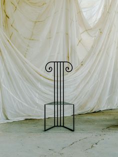 an iron table with a glass top in front of a curtain