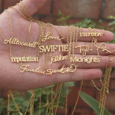 a person's hand holding several different types of necklaces with names on them