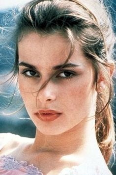 a beautiful young woman in a white dress posing for a photo with her hair blowing in the wind