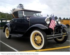 an old model t car is parked in a parking lot with an american flag on it