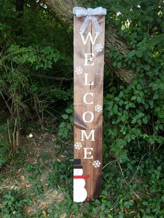 a wooden welcome sign with snowflakes on it in front of some bushes and trees