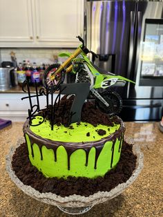 a cake with green icing and a dirt bike on top is sitting on a counter