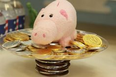 a stuffed pig sitting on top of a pile of coins and gold coins in a bowl