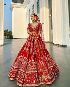 a woman in a red and gold bridal gown posing for the camera with her hand on her hip