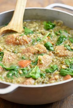 a pot filled with meat and vegetables on top of a wooden table next to a spoon