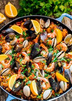 seafood paella in a blue skillet with lemon wedges and parsley on the side