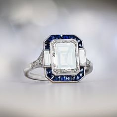 This item has just been reserved by another customer. Please contact us to be notified if it becomes available.  This stunning platinum engagement ring features an emerald cut diamond weighing approx 3.05 carats, L color, and VS1 clarity. The center diamond is bezel-set, surrounded by a halo of French-cut natural sapphires and baguette-cut diamonds. Diamond-set shoulders lead past an openwork under-gallery. This ring is decorated with fine milgrain. ✦ DIAMOND SPECIFICATIONS:  Center Diamond Weig Geometric Engagement Ring, Engagement Ring With Halo, Sapphire Engagement Ring Halo, Sapphire Halo Ring, Estate Diamond Jewelry, Emerald Cut Diamond Engagement Ring, Emerald Cut Diamond Engagement, Asscher Cut Diamond, Emerald Cut Diamond