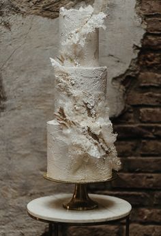 a three tiered white wedding cake on top of a small table with a brick wall in the background