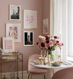 a dining room with pink chairs and pictures on the wall above it, along with flowers in vases