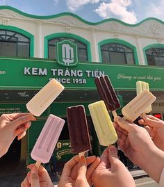 several people holding ice cream on sticks in front of a green and white building with the words kem trang tien