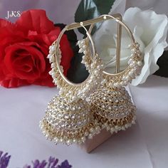 a pair of gold and white beaded earrings on a stand next to a rose