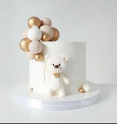 a white cake with gold balloons and a teddy bear