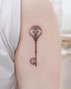 a small key tattoo on the back of a woman's left arm and shoulder