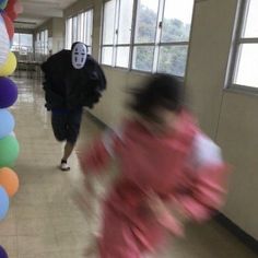 two children are running down the hall with balloons in front of them and one is wearing a mask