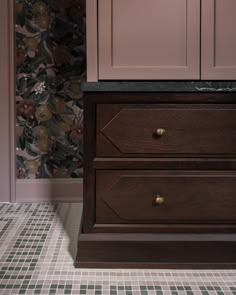 a dresser with two drawers in front of a floral wallpaper