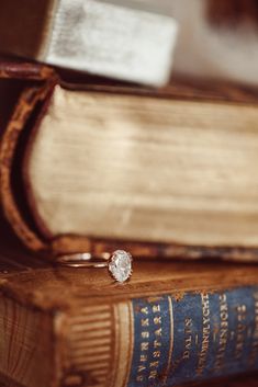 a diamond ring sitting on top of an old book next to a stack of books