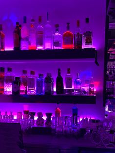 the shelves are filled with different types of liquor bottles and glasses in purple lighting behind them