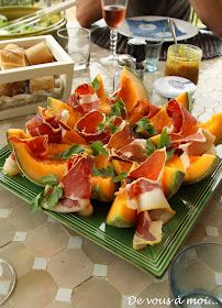 a green plate topped with slices of melon covered in prosciutto