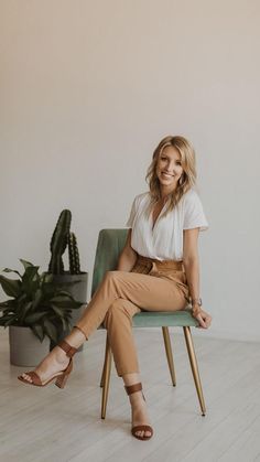 a woman is sitting on a chair in front of a potted plant and smiling