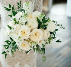 a bridal holding a bouquet of white flowers and greenery in it's hands