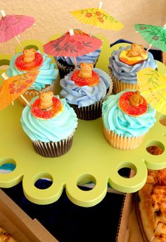 cupcakes with blue frosting and colorful toppings on a yellow tray next to pizza