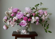 a vase filled with pink and white flowers sitting on top of a wooden table next to a wall