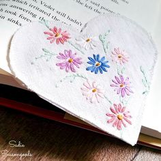 an open book with embroidered flowers on it and a heart - shaped object in the middle