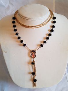 "This handmade Black Faceted Glass Beaded Rosary Necklace features 3 Strands of a gold tone curb chain added to a jump ring that is connected to an individual beaded connector. At the bottom a Silver Tone Oval Medal with La Virgen De Guadalupe is added. The medal double sided with dangling chains and 3 beaded connectors. All items used are new non are vintage. This Religious Virgen De Guadalupe Necklace will arrive in a gift box with FREE SHIPPING. Measures: 32\" Long But Doubled so Half of that Vintage Gold Beaded Necklace With Adjustable Chain, Gold Metal Beaded Necklaces With Black Beads, Gold Metal Beaded Necklace With Black Beads, Adjustable Gold Beaded Necklace With Chain, Gold Metal Necklace With Black Beads, Gold Multi-strand Necklace With Black Beads, Spiritual Gold Necklace With Black Beads, Mexico Birthday, Guadalupe Necklace