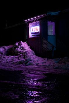 a purple light shines on the side of a building in the snow at night