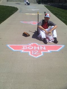 a man sitting on the sidewalk with a baseball bat in his hand and some chalk drawings behind him