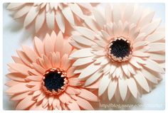 three pink flowers with black centers on a white table top, one is cut in half and the other two are made out of paper