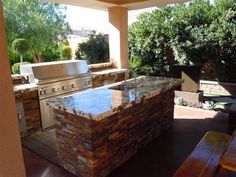 an outdoor kitchen with stone counter tops and stainless steel appliances