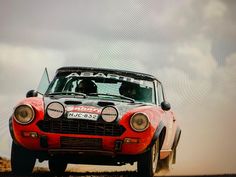 an old red car driving down a dirt road