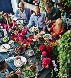 a group of people sitting around a table with plates and food on it, surrounded by flowers