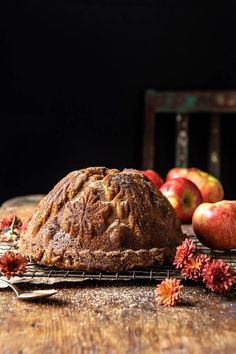 a loaf of bread sitting on top of a wooden table next to apples and flowers