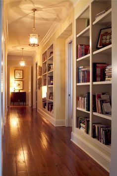 an empty hallway with bookshelves and lamps on either side of the room,