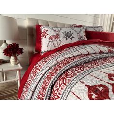 a bed with red and white comforters on top of it in a room next to a lamp