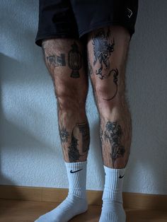 the legs and ankles of a man with tattoos on his body, standing in front of a wall