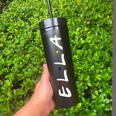 a hand holding a black tumbler with the word efl on it in front of some bushes