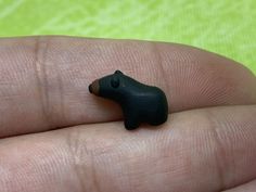 a tiny black bear figurine sitting on top of a persons finger in front of a green background