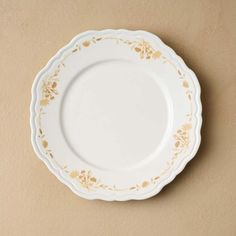 an empty white plate with gold designs on it's rim against a beige wall