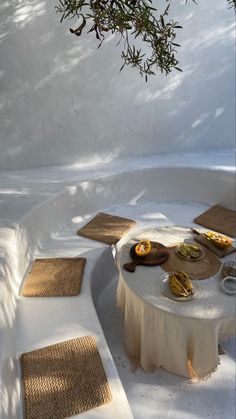 an outdoor table with food on it under a tree in the snow, surrounded by steps