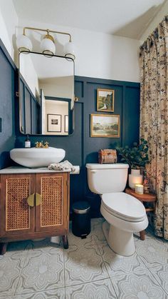 a white toilet sitting next to a sink in a bathroom under a mirror above a wooden cabinet