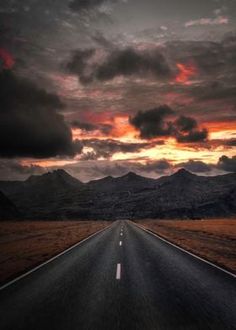 an empty road in the middle of nowhere with mountains in the background at sunset or dawn