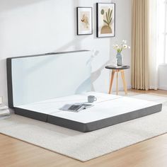 a white bed with a gray mattress on top of it next to a wooden floor