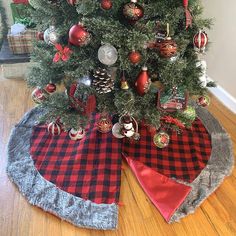 a christmas tree with ornaments on it and a red ribbon around the base is sitting on a wooden floor