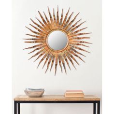 a table with a bowl and mirror on it next to a wall mounted sunburst