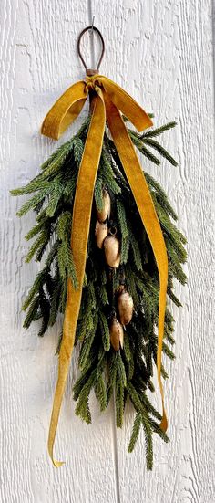 a christmas wreath hanging on the side of a white building with yellow ribbon and pine cones