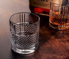 an empty glass sitting on top of a wooden table next to a bottle of whisky