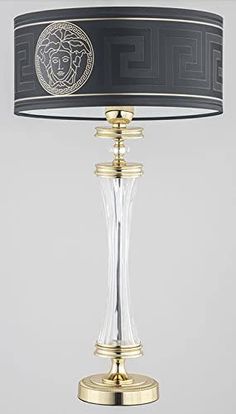 a table lamp with a black shade on it and a golden base, in front of a gray background